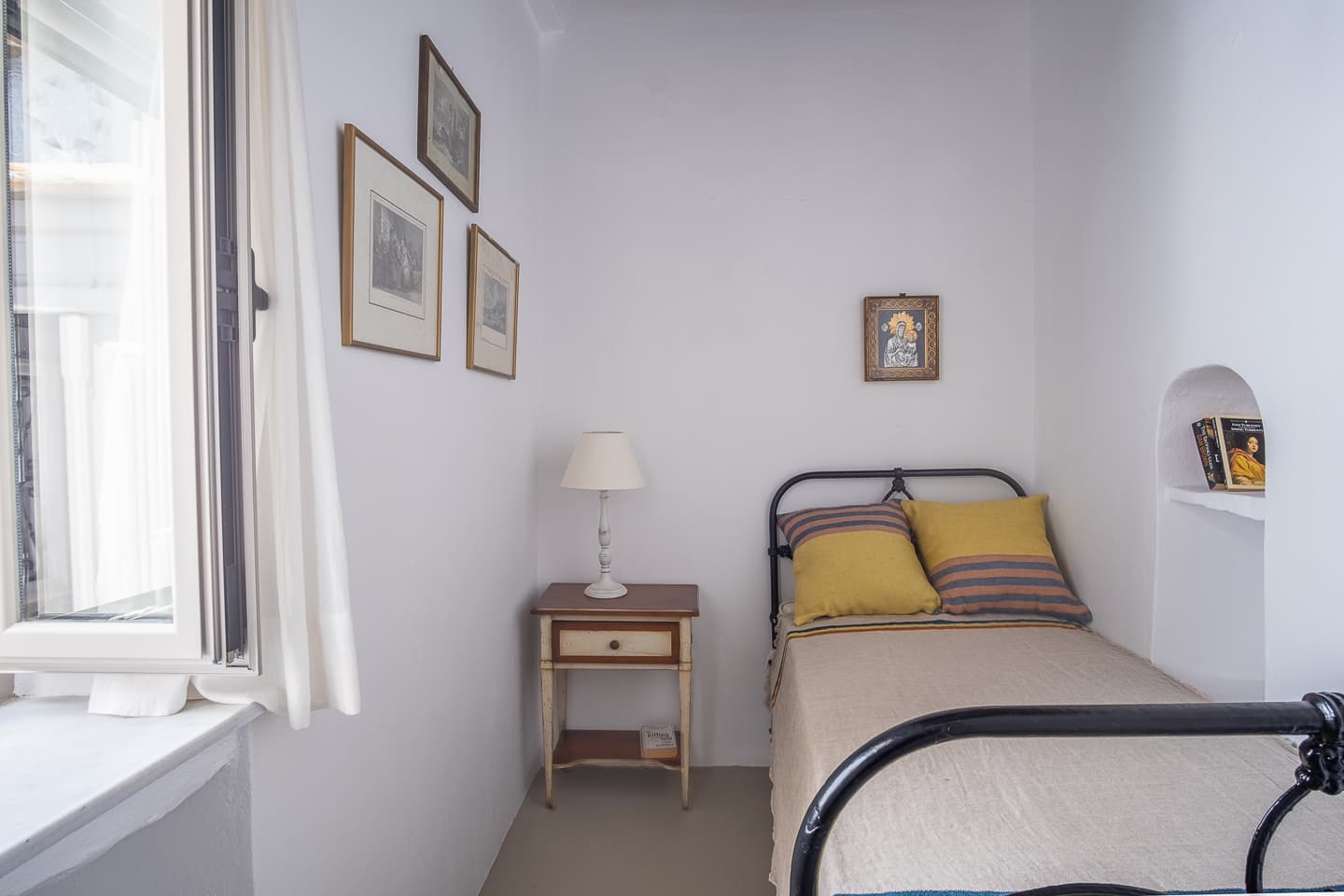 One of the two single bedrooms at Casa di Lavalle, with a wrought-iron bed frame and framed prints on a whitewashed wall.