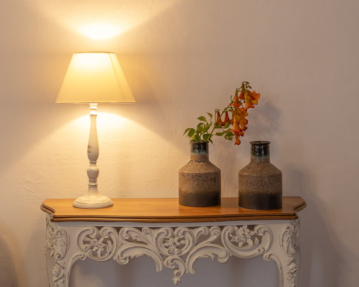 A carved console table at Casa di Lavalle dressed with a ceramic lamp and stoneware vases of trumpet vine, against a plastered wall.