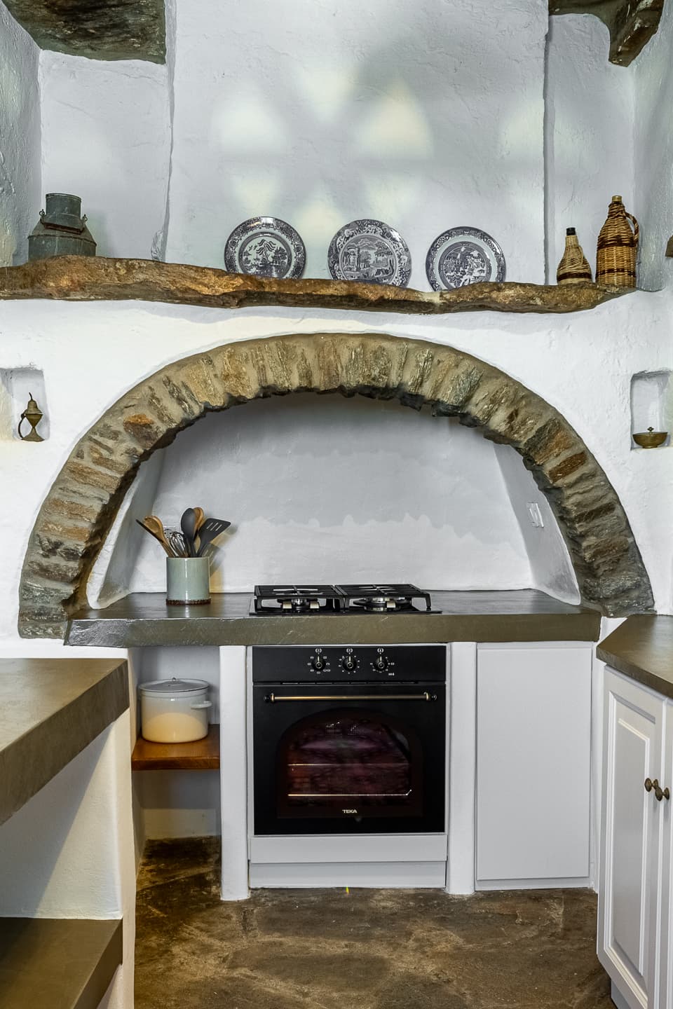 A stone-arched hearth niche in the Casa di Lavalle kitchen, with a built-in gas hob and oven beneath a mantel of antique blue-and-white plates.