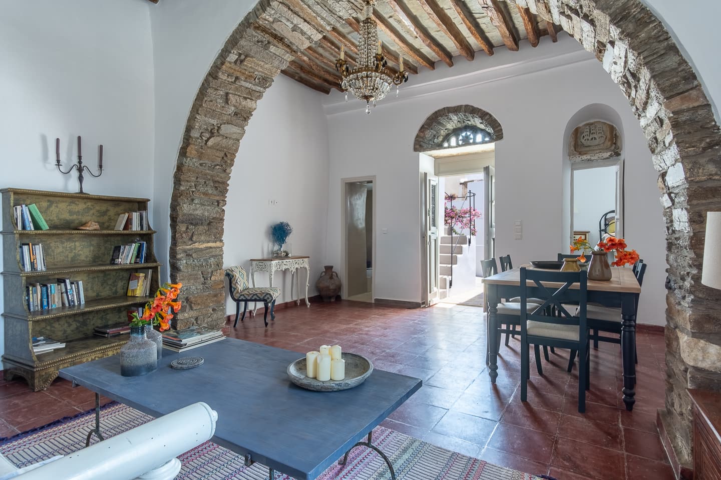 A stone archway at Casa di Lavalle opens onto the dining table for six beneath a timber-and-stone ceiling, with a weathered bookcase to one side.